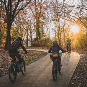 Three individual riding a paved trail at sunset