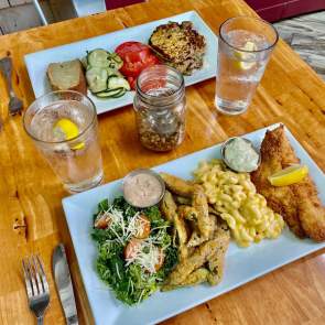 two plates of food on a table - fish, mac and cheese, fries, greens