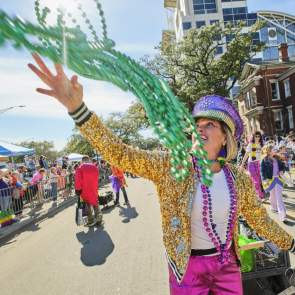 A Mardi Gras reveler in gold sequins and hot pink pants throws green beads to a crowd