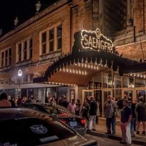 building with lighted entrance at night, people and cars outside