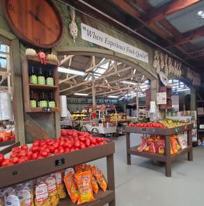 Inside the LJB farmhouse store, showing fresh tomatoes apples, olive oils, garlic braids, and bagged chips.