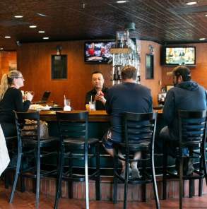 people sit at a horseshoe-shaped bar in a restaurant while a bartender makes drinks