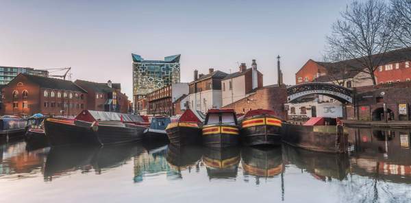 Canal boats moored at Gas Street Basin Birmingham in front of bring building a a large cubed glass building behind