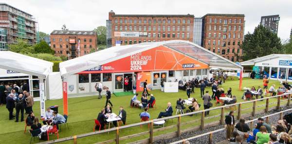 The outside of the West Midlands Pavilion at UKREiiF 2024. Guests network and enjoy a drink on the green in front of the stand.
