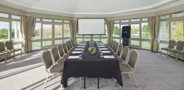 A long boardroom table in a premium room, surrounded on three sides by large windows.
