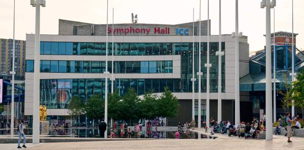 The ICC and Symphony Hall building seen across Centenary Square in Birmingham, with people milling about in front of the building.