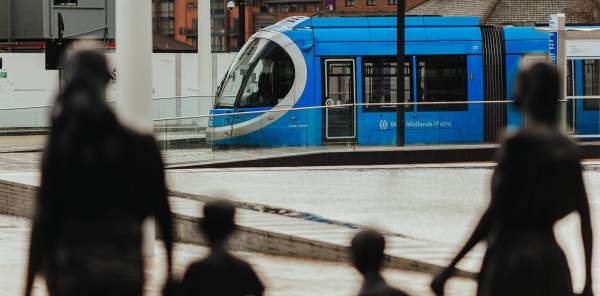 A tram is seen in the distance, past the silhouette of a family of statues