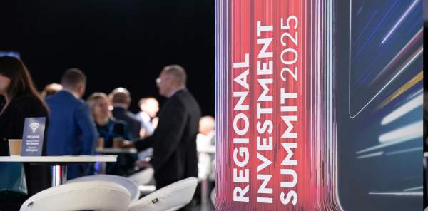 A sign for the Regional Investment Summit 2025 with people talking in the background