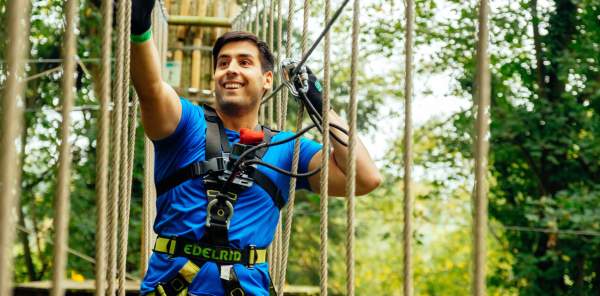 A man crosses a rope bridge high in the trees at Bear Grylls Adventure