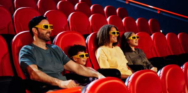 A man, his wife, and children sit in cinema seats wearing 3D glasses