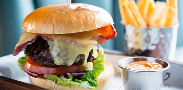 Close up photo of a stacked cheeseburger on a plate, alongside ranch dressing and fries