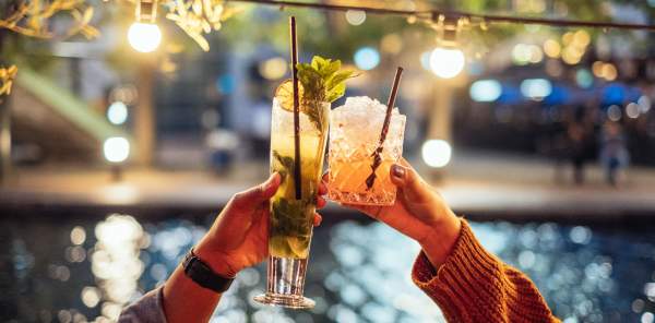 Two people raising cocktails in the air to cheers