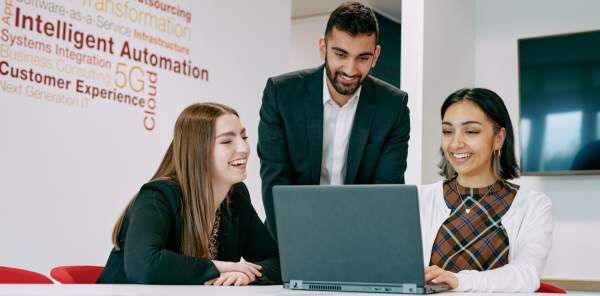 Three business people look at a laptop screen, having reached a conclusion they all agree on