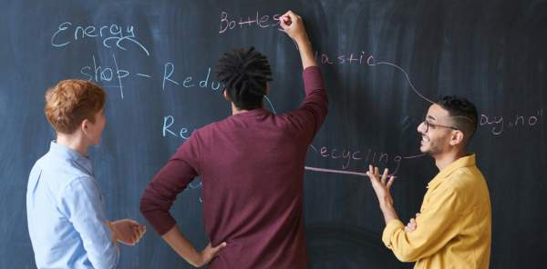 Three people work together to create a plan on a blackboard