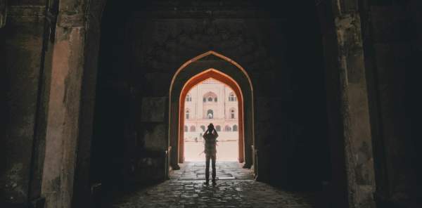 A tourist stands silhouetted in a bright archway at a historical site.