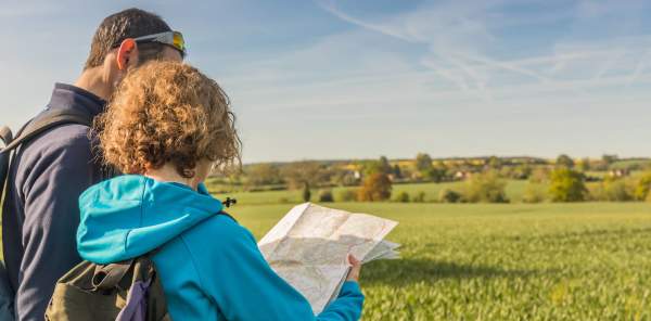 Man and lady exploring through green field with a map in hand