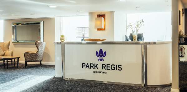 A reception desk at the Park Regis hotel, bearing it's name in bold letters