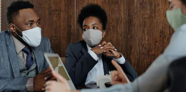 Business people hold a discussion around a table while wearing face masks