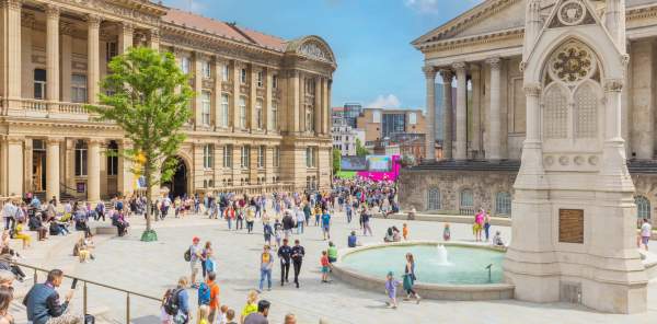 Groups of people sitting outside in summer clothes. Surrounded by Chamberlain Square fountain and Birmingham Museum and Art Gallery