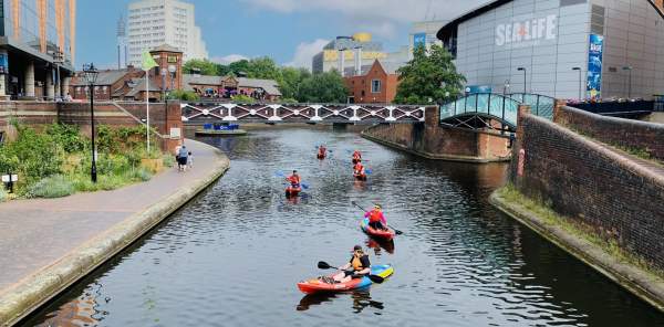 Group of people kayaking at Round House Birmingham with Sea Life Centre and Library of Birmingham in the background