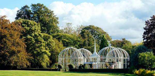 The Botanical Gardens, showing an elaborate greenhouse in the distance across a wide open, green space, framed by large trees.