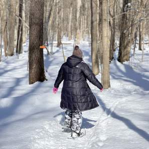 Woman snowshoeing at Beaver  Lake nature center, she's walking away from the camera