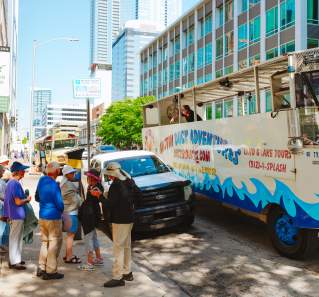 People line up on the sidewalk outside of the Austin Visitor Center waiting to board the Duck Tour vehicle