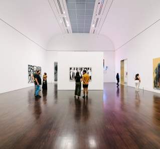 People admiring an art exhibit in a large white room at the Blanton Museum of Art.
