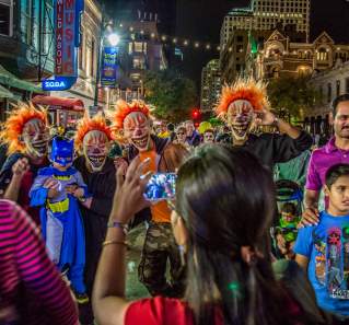 Woman takes photo of four men in clown masks with children for Halloween on Sixth Street in Austin Texas