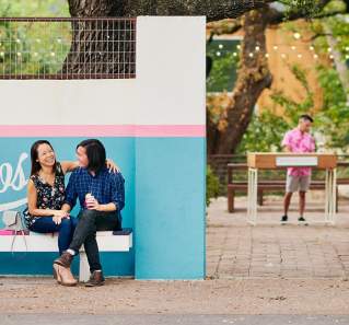 Couple sitting in front of Bienvenidos sign under live oak tree at Fresas outdoor patio in Austin Texas