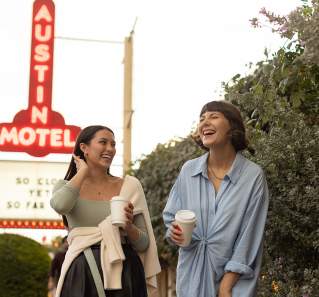 Two women walking and laughing on South Congress Avenue. Austin Motel neon sign is lit up in background