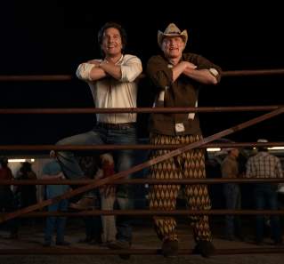 Matthew McConaughey and Woody Harrelson leaning on a livestock gate at a rodeo.