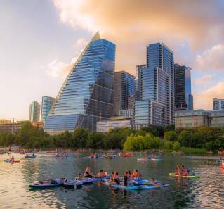 Image of people kayaking on Lady Bird Lake with the downtown skyline in the background.