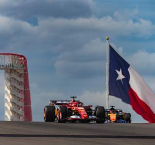Image of a formula 1 car on the track at Circuit of the Americas with the tower and a large Texas flag in the background.