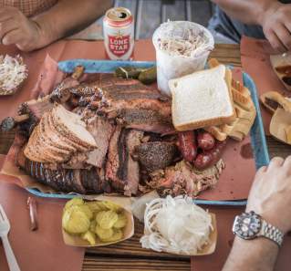 three men sit around a platter of BBQ and sides at Franklin Barbecue in Austin Texas