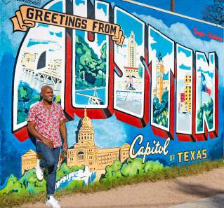 Man in patterned shirt leaning against the "Greetings from Austin" postcard mural.