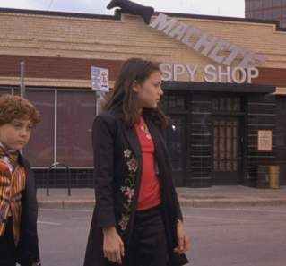 Spy Kids screengrab showing Carmen and Juni walking together in front of a building with sign reading Machete Spy Shop