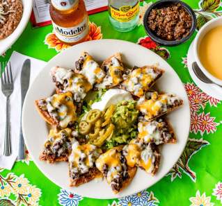 Mandito's Beef Nachos with sour cream, guacamole and jalapenos on a plate next to a bowl of queso, a modelo beer and a topo chico