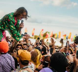 Musician reaching into crowd of people surrounding a stage.