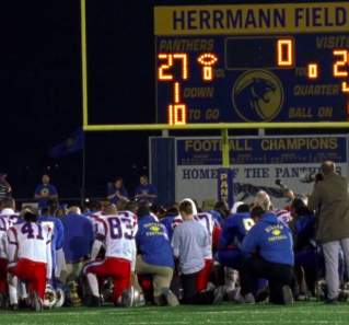 Friday Night Lights Screengrab showing a football team kneeling on Herrmann Field in front of a goal with scoreboard showing score of 27 to 24