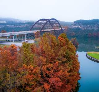 View of Lake Austin lined with fall-colored trees and the Penny Backer Bridge against a foggy Hill Country.