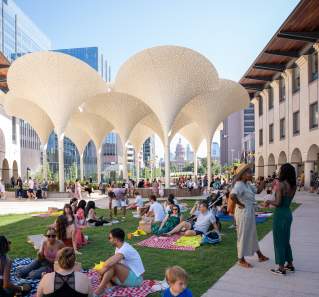 Groups of people standing around and sitting on picnic blankets across the Blanton Museum's lawn, in between museum buildings.