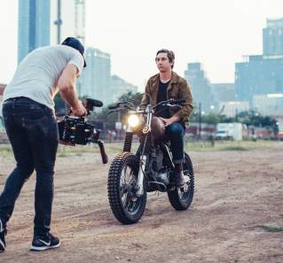 Man filming a young man on a motorcycle with the Austin skyline in the background.