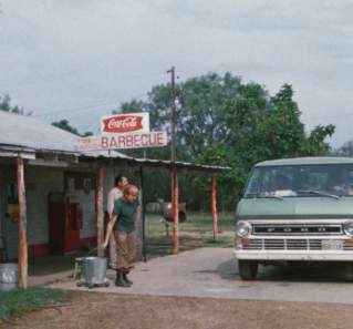 Texas Chainsaw Massacre screengrab, showing a green van parked in front of a gas station with a coca cola and Barbecue sign. Two men walk towards the van