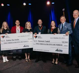 Two women and two men on a stage holding a giant check for scholarship recipient.