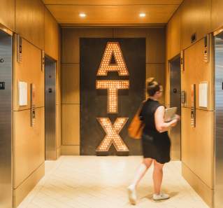 Woman walking into an elevator, passing by a large ATX sign in an elevator atrium.