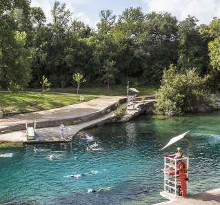 Historic Barton Springs Pool with several people swimming through the clear water and a lifeguard on duty