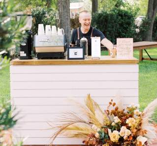 Man standing behind an event bar happily making specialty lattes.