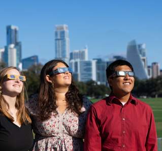 Three people looking at the sun wearing eclipse glasses in Zilker Park.