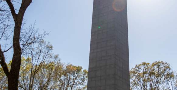 A tall stone tower with metal plaques at the base in the middle of a forest
